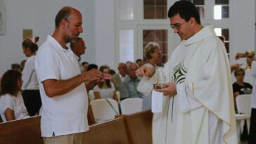 Priest distributing communion during a Catholic mass with congregation present.