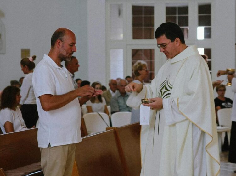 Priest distributing communion during a Catholic mass with congregation present.