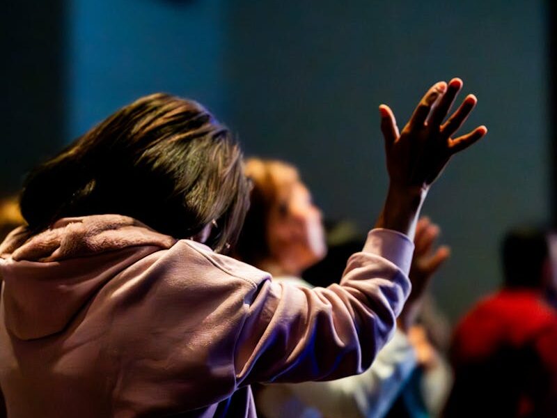A group of people raising their hands in a spiritual gathering, immersed in prayerful worship.