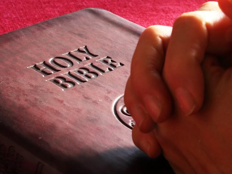 Close-up of hands praying on a Holy Bible, symbolizing faith and spirituality.
