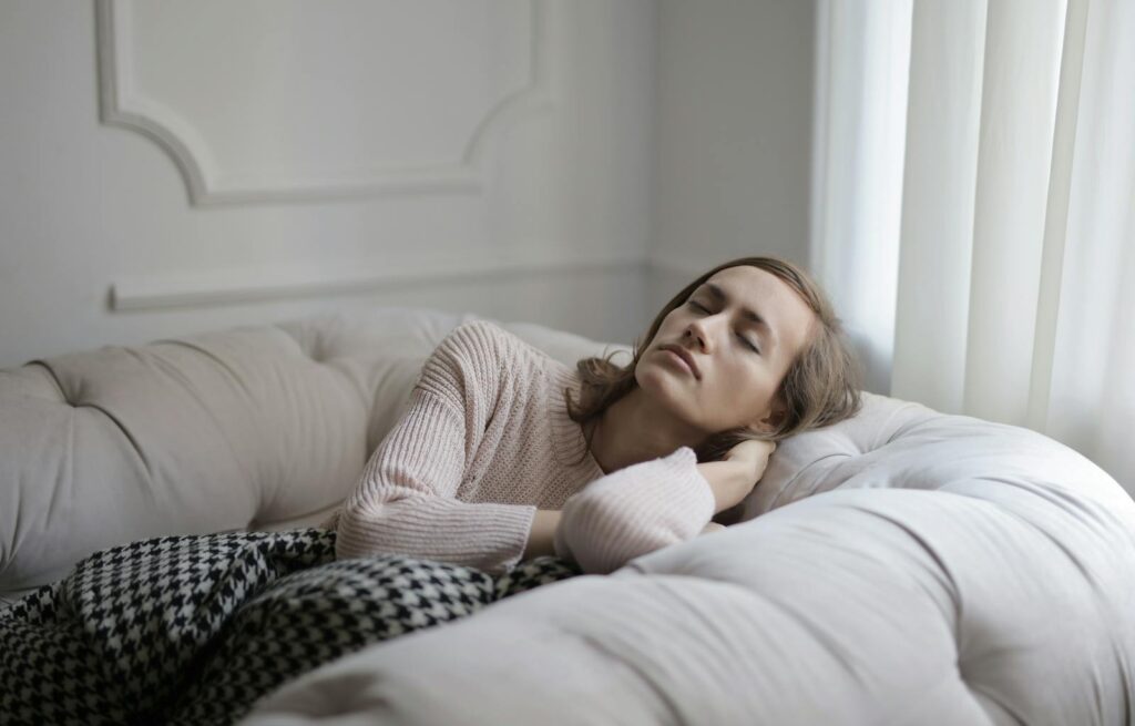 A woman in a cozy sweater relaxing on a sofa with eyes closed, conveying a sense of peace.