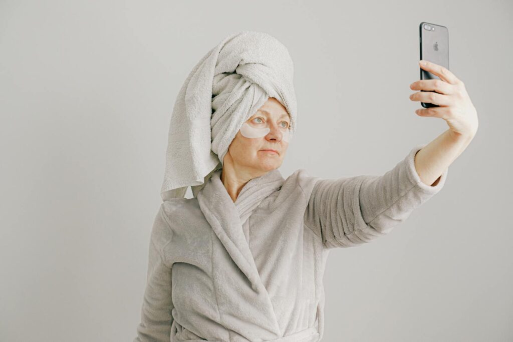 Mature woman in bathrobe taking a selfie using smartphone indoors.