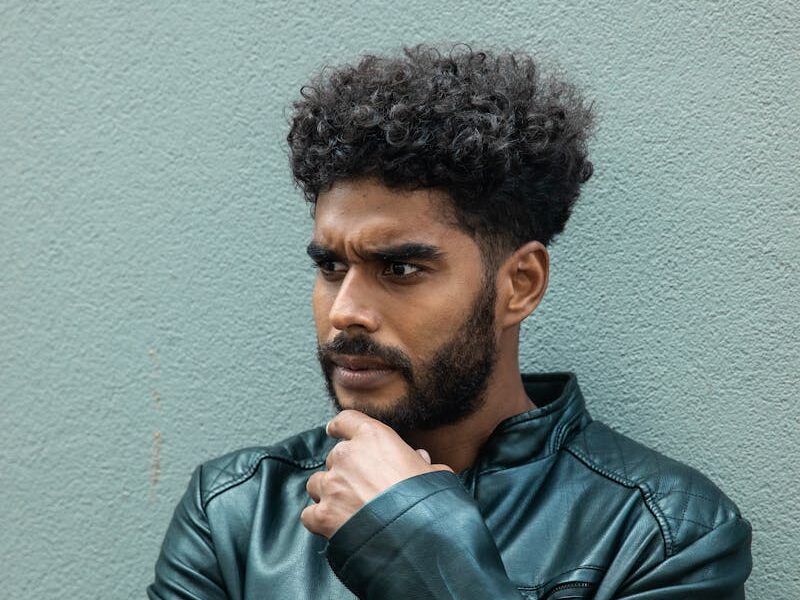 African American man in a leather jacket looking thoughtful against a neutral background.
