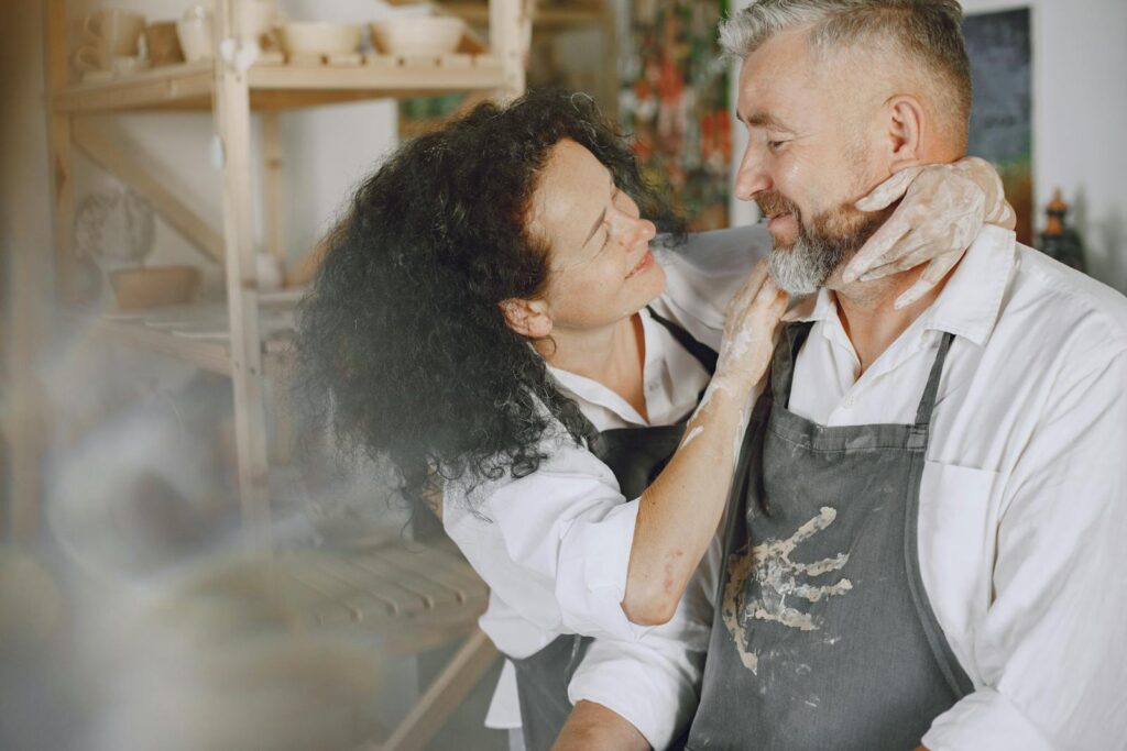 Loving couple smiling at each other in a pottery studio, embracing in artistic surroundings.