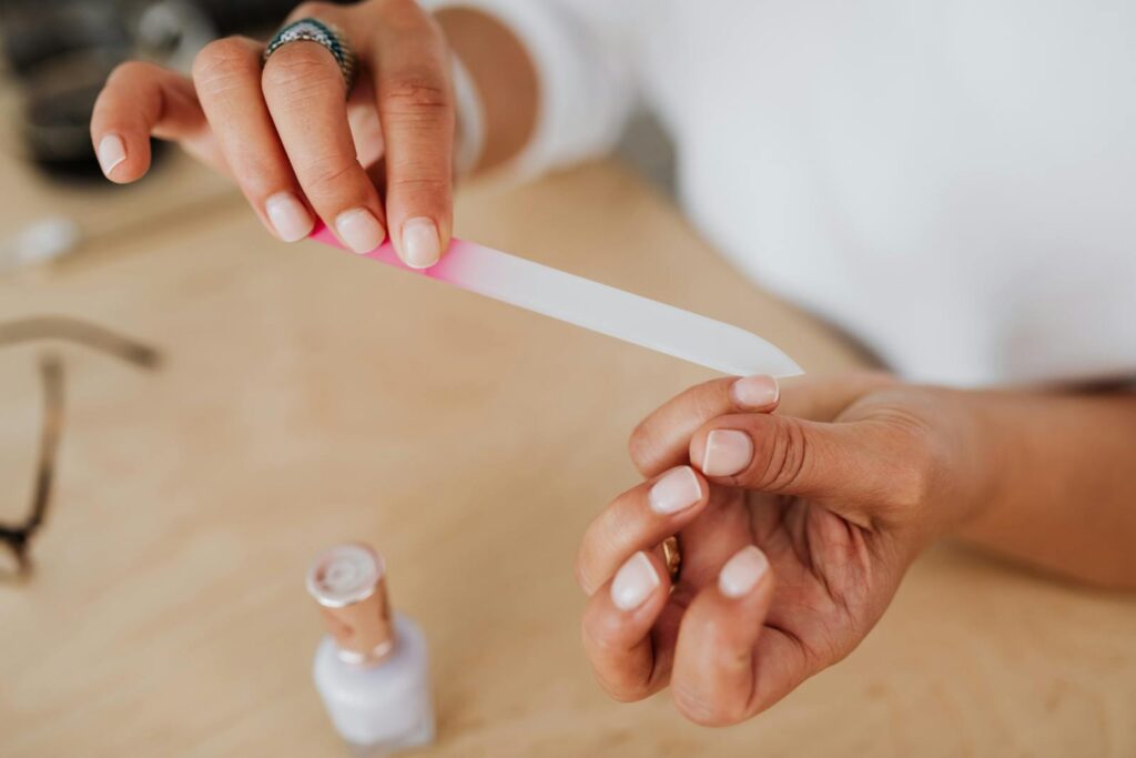 Detailed view of hands filing nails with a nail polish bottle nearby, showcasing personal grooming.
