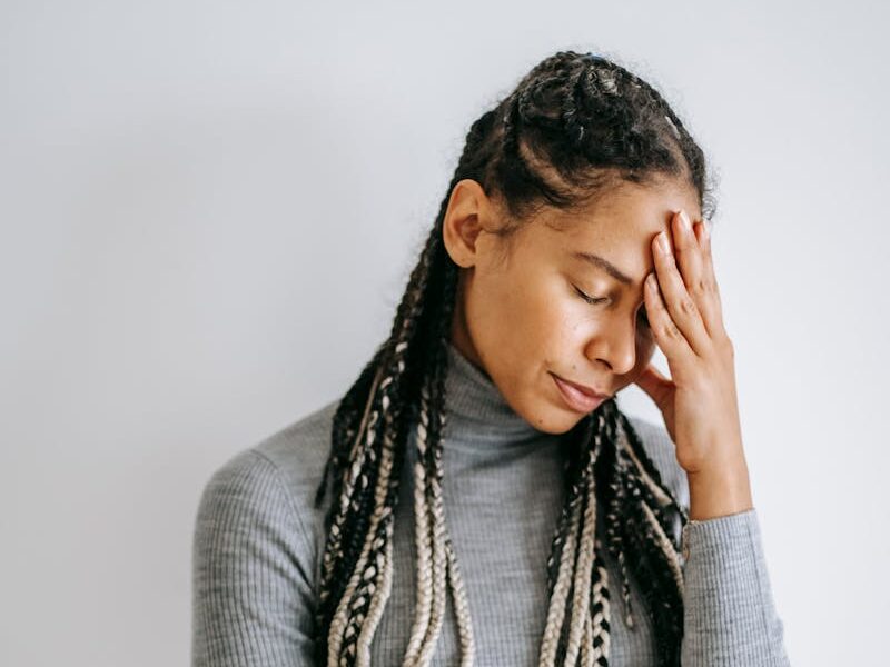 Young woman stands with a hand on her forehead, expressing thoughtfulness or mild tension.
