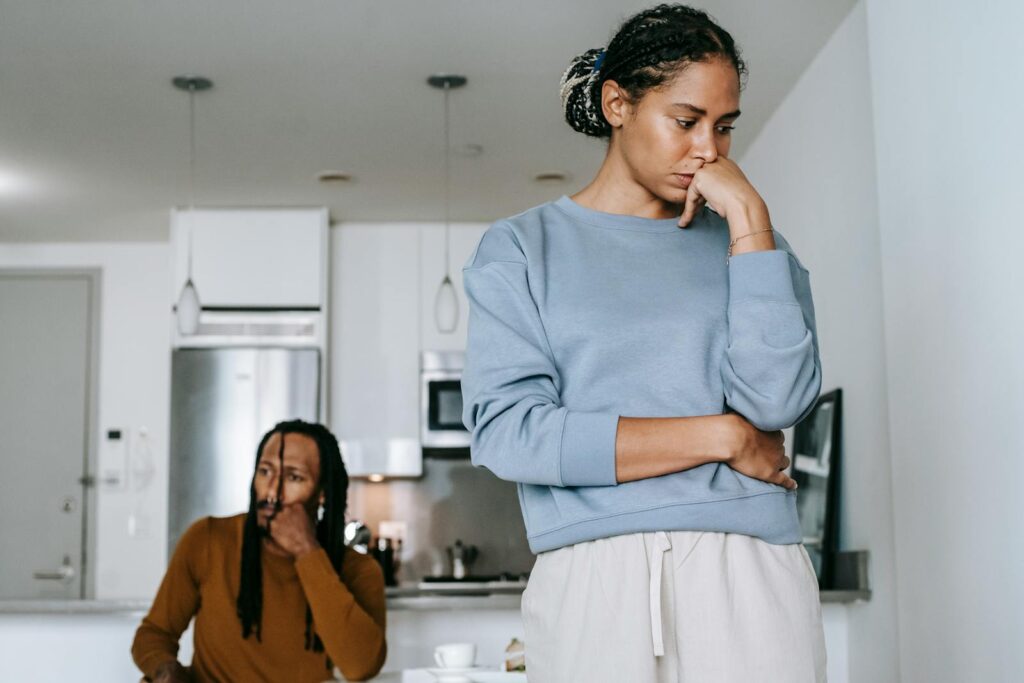 From below of young displeased African American female touching face near pensive boyfriend during conflict in kitchen