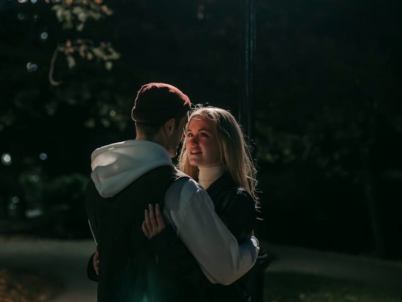 A couple sharing a romantic moment under a streetlamp in a city park at night.