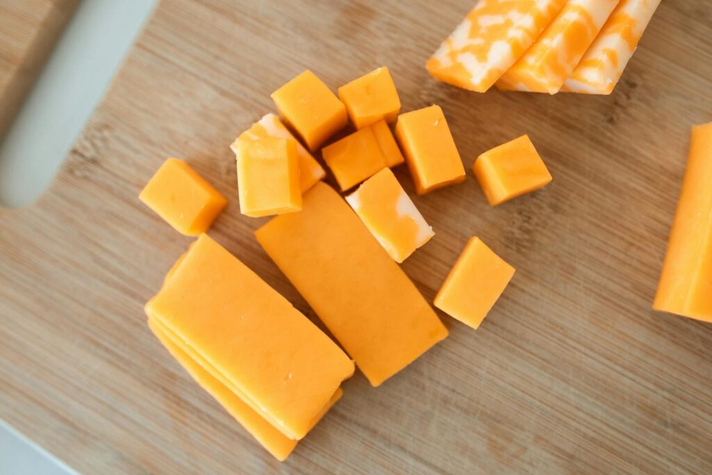 Close-up of cheddar cheese cubes and blocks on a wooden cutting board.