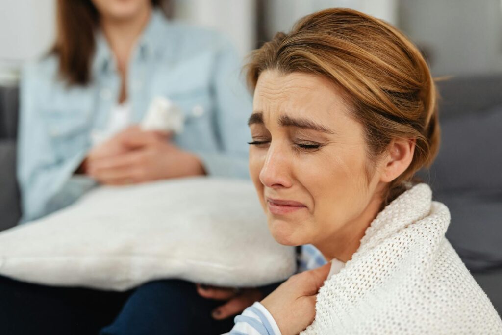 Caucasian woman crying and being comforted by a friend indoors.