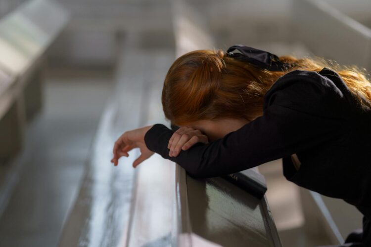 A redheaded woman in deep prayer, leaning on a church pew in a serene atmosphere.