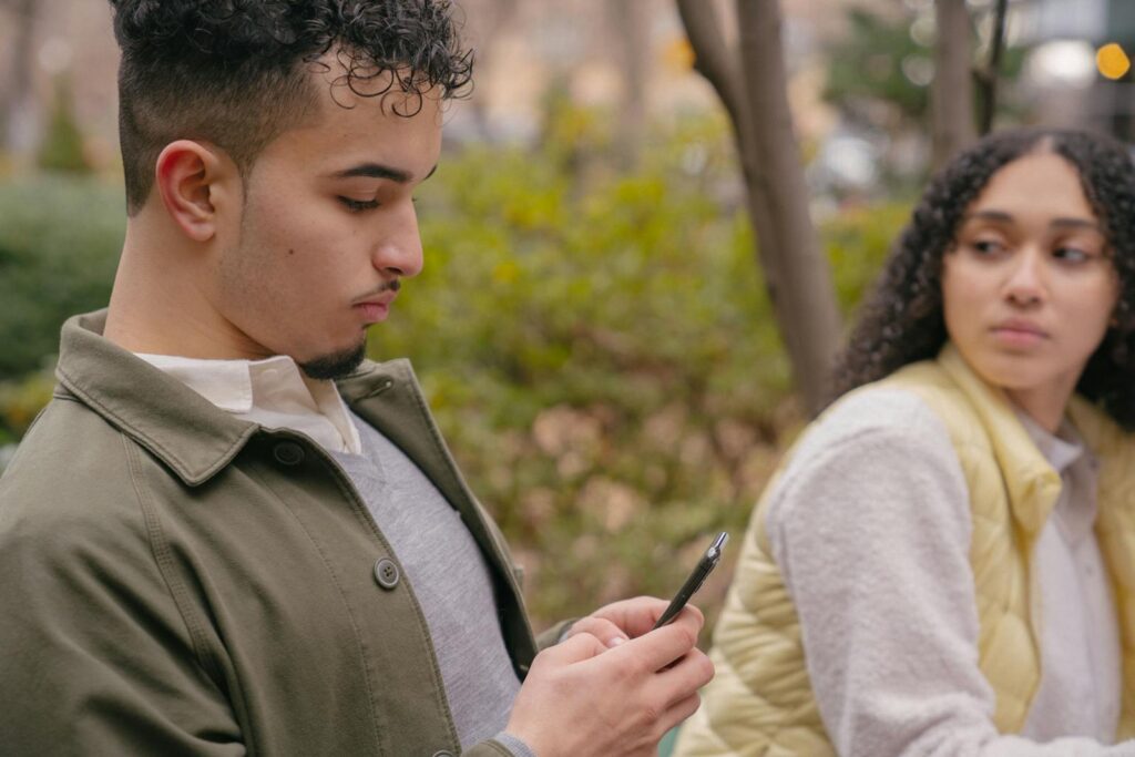 A young couple sitting outdoors with a smartphone, capturing casual moments and emotions.