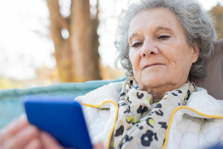 Elderly woman with a smartphone relaxing outdoors in autumn.