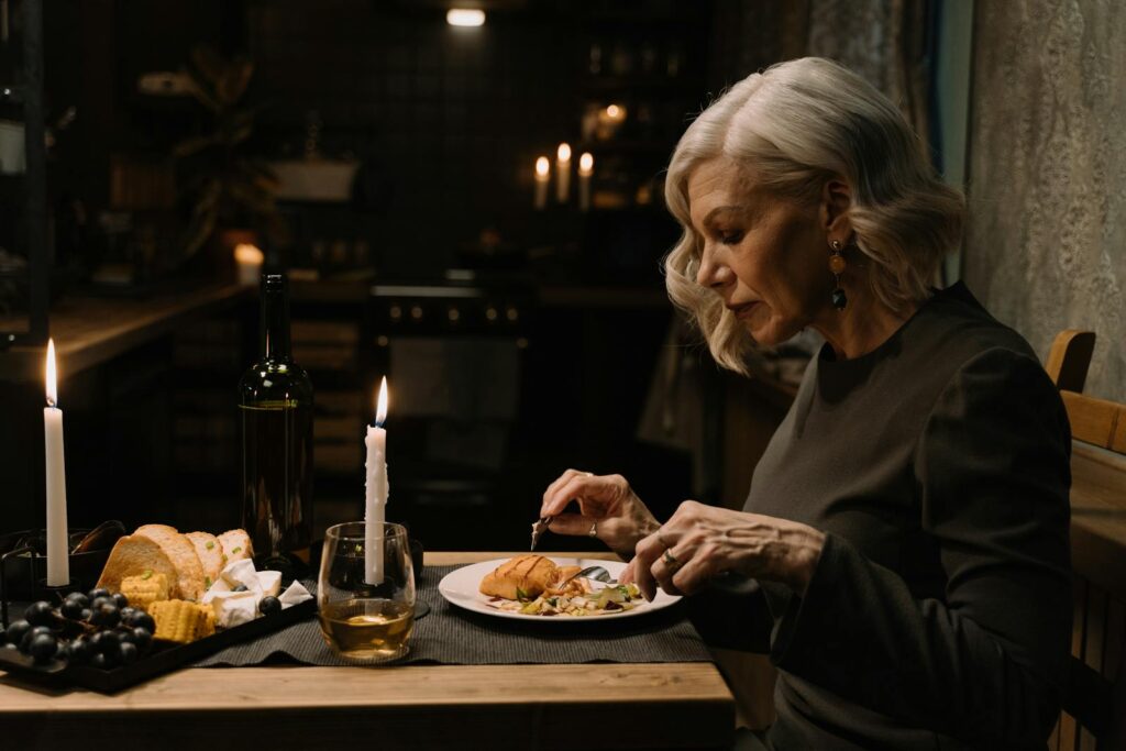 Senior woman enjoying a candlelit dinner alone indoors with wine and cheese platter.