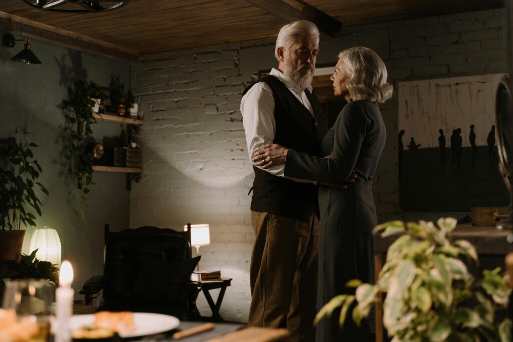 Elderly couple enjoy a dance in their warmly lit home surrounded by plants.