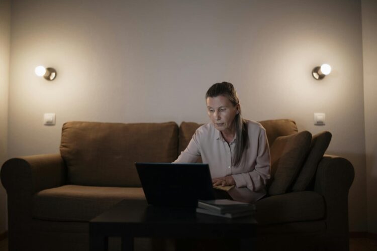 A senior woman focused on her laptop in a cozy, well-lit living room setting.