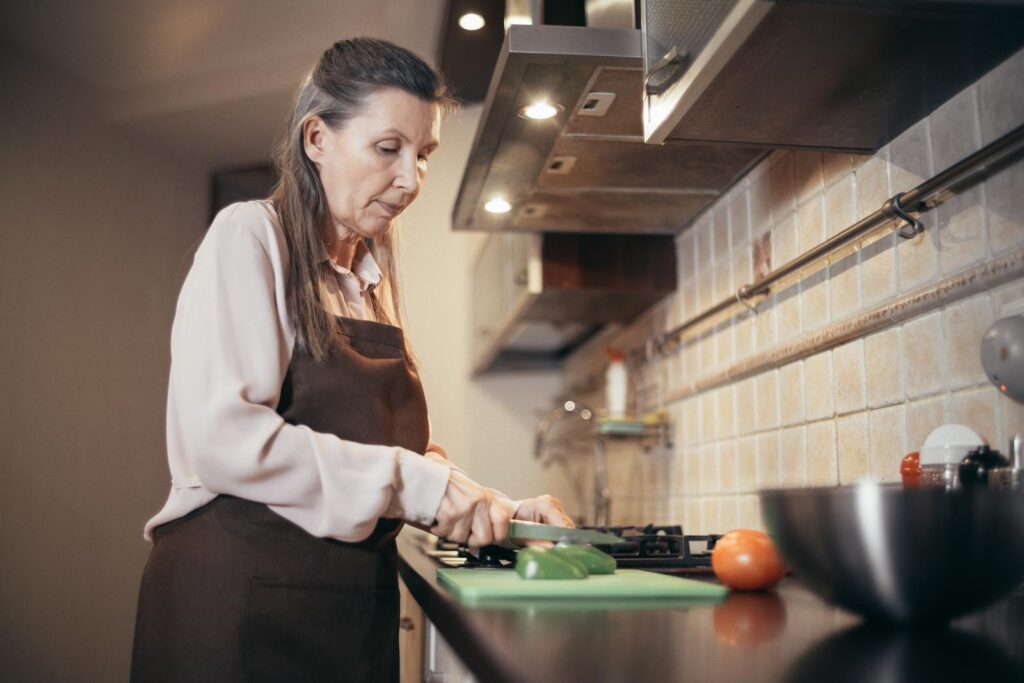 Senior woman chopping vegetables in a warm, cozy kitchen setting. Engaged in daily home cooking.