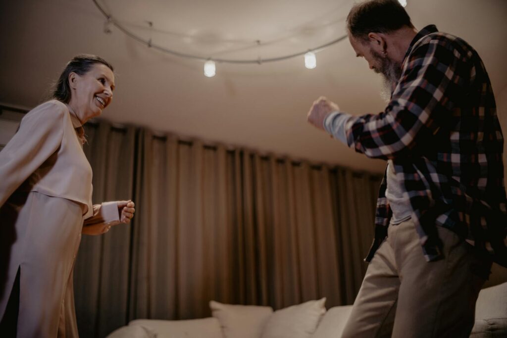 A lively senior couple dancing indoors with smiles, enjoying a joyful moment together.