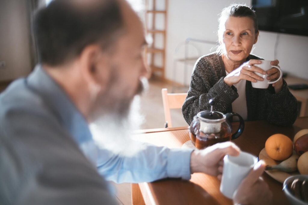Elderly man and woman sharing a coffee moment in a cozy indoor setting.