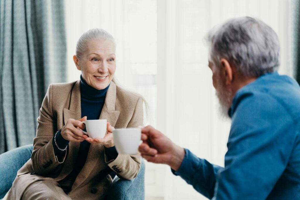 Senior couple enjoying coffee indoors, smiling and engaged in conversation, creating a warm, inviting atmosphere.
