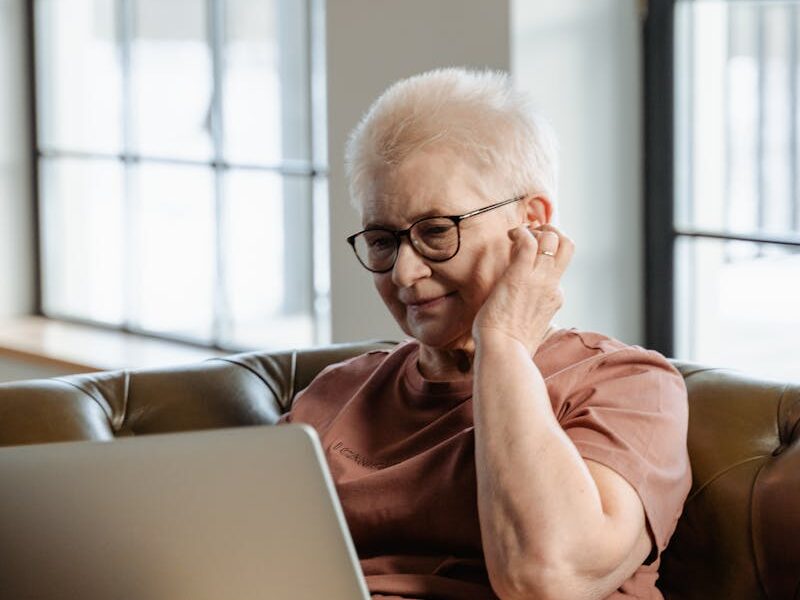 Elderly woman engaging with laptop indoors, enjoying online leisure activities.