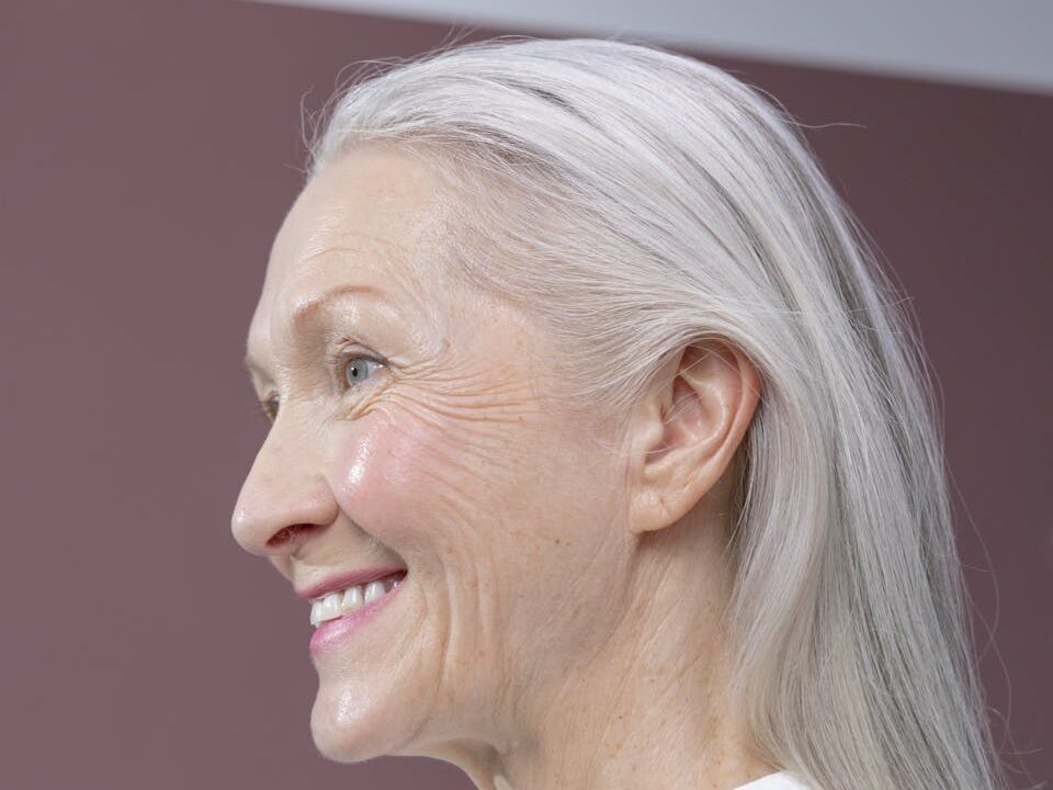 Portrait of a senior woman with gray hair, smiling in profile against a simple background.
