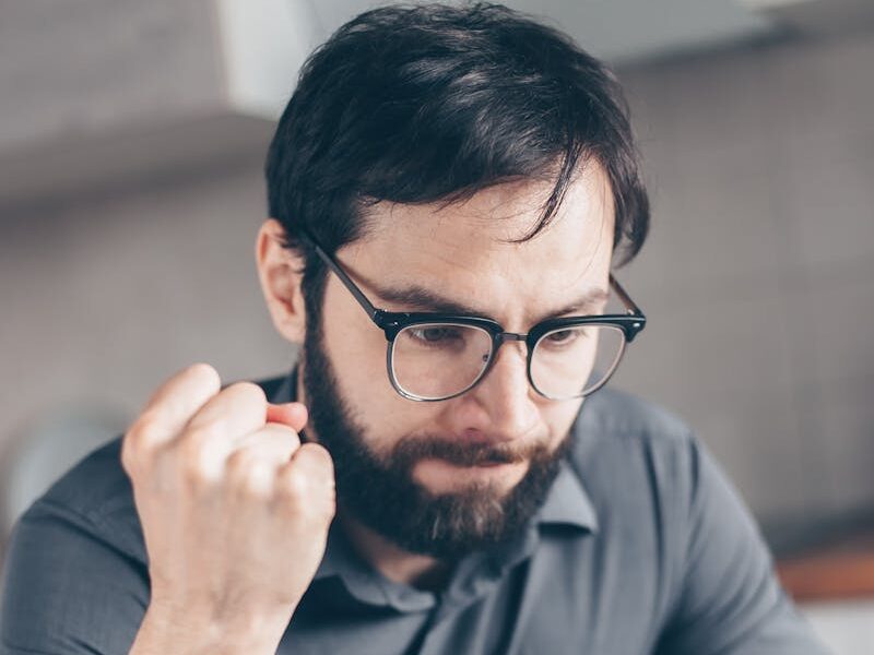 Angry man in glasses reads paperwork intensely at indoor desk.