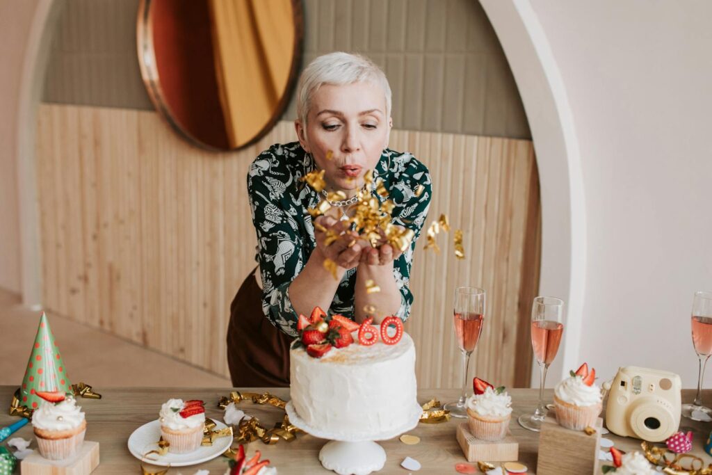 A joyful elderly woman blowing confetti at her 60th birthday party with cake and champagne.