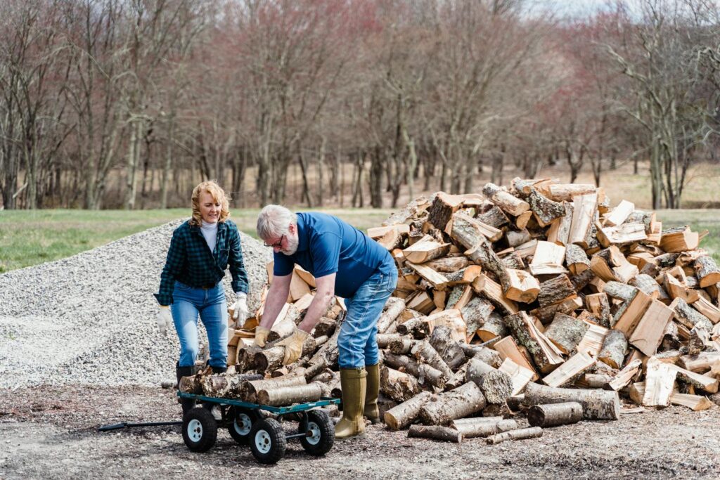 Mature couple working together to load chopped firewood onto a cart in a rural outdoor setting.