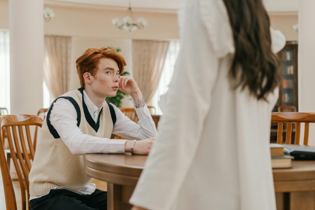 Red-haired student in a library, seated at a table, engaged in a thoughtful discussion.