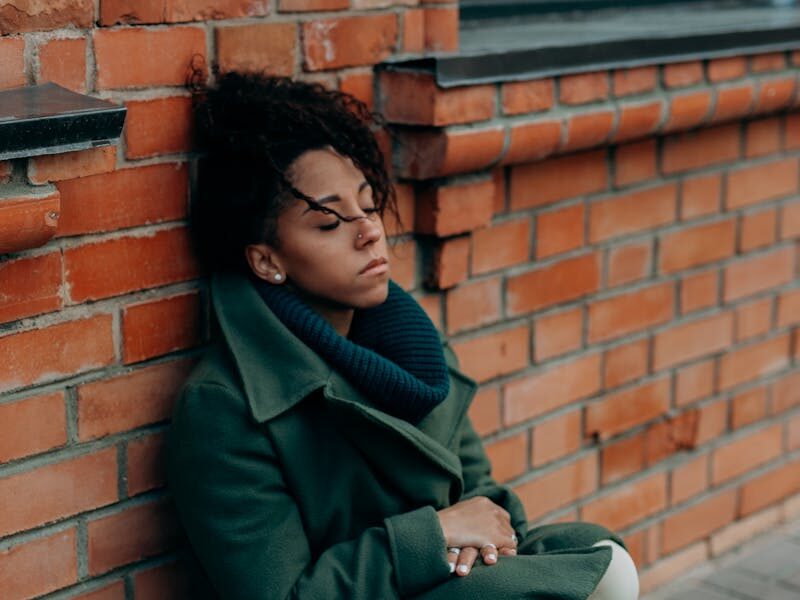A contemplative woman leans against a brick wall, embodying solitude and introspection.