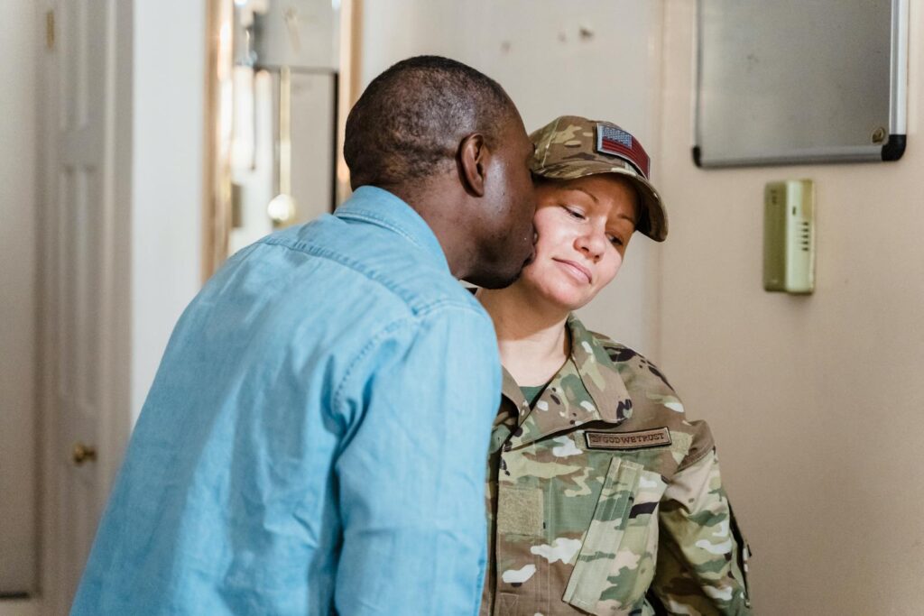 A couple shares an affectionate moment as one partner kisses the cheek of the other in military uniform.