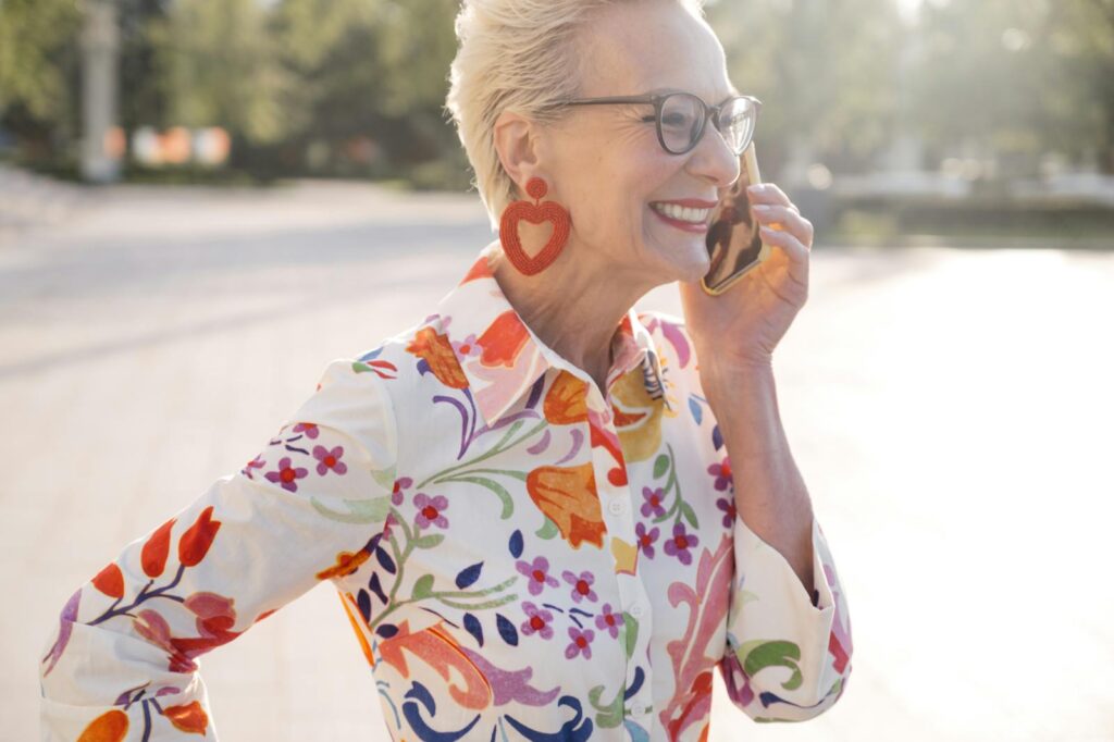 Senior woman with stylish glasses and floral shirt smiling while on a call outdoors.
