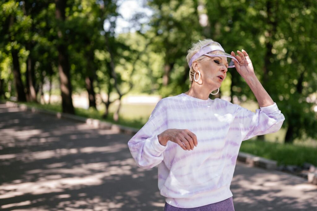Senior adult woman outdoors in a park taking a break during a workout, wearing casual sportswear.