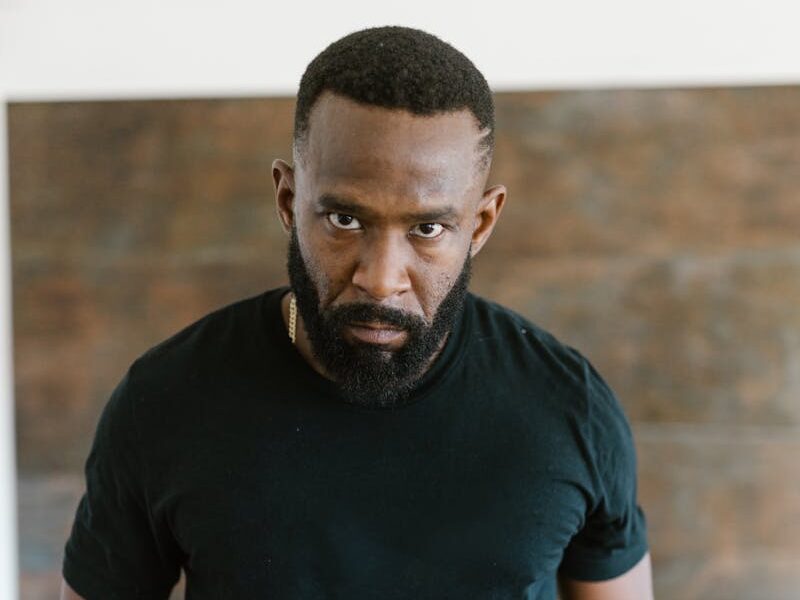 Portrait of a muscular man with a strong expression, wearing a black t-shirt indoors.