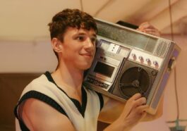 Smiling teenager holding a vintage boombox, embracing retro 80s vibes indoors.