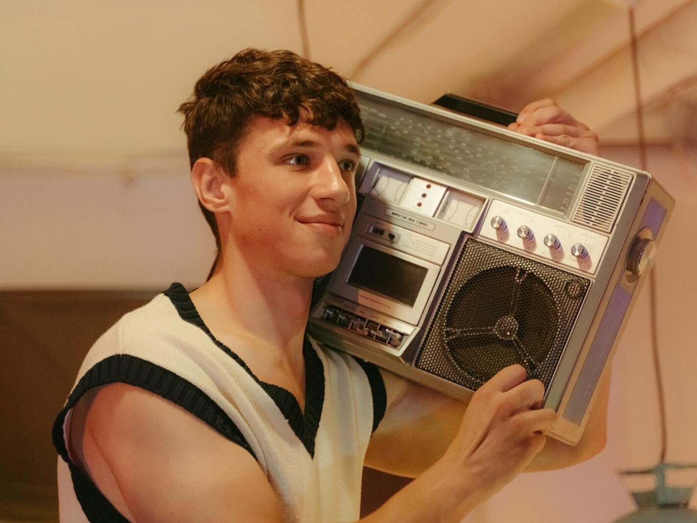 Smiling teenager holding a vintage boombox, embracing retro 80s vibes indoors.