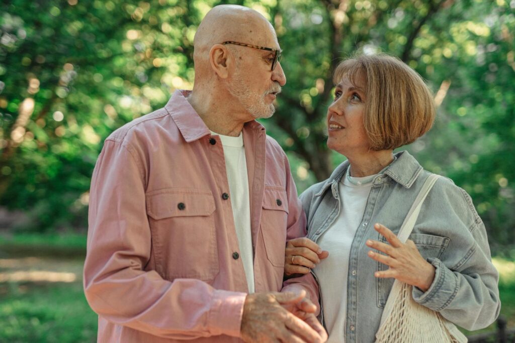 An elderly couple shares a joyful conversation in a vibrant green park setting.