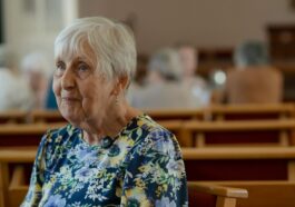 An elderly woman sits in church.