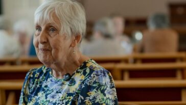 An elderly woman sits in church.
