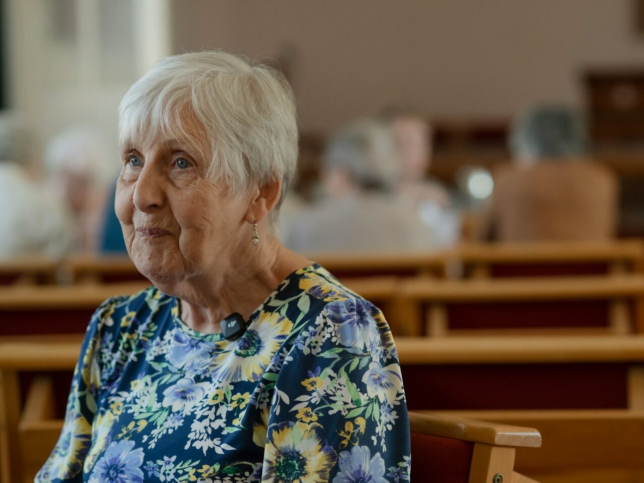 An elderly woman sits in church.