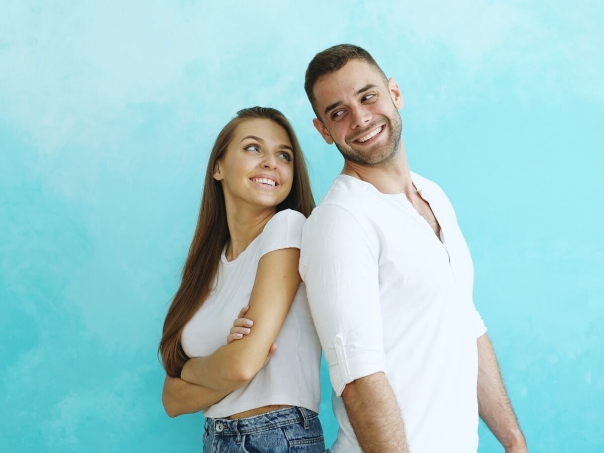 Couple smiling back to back against blue wall