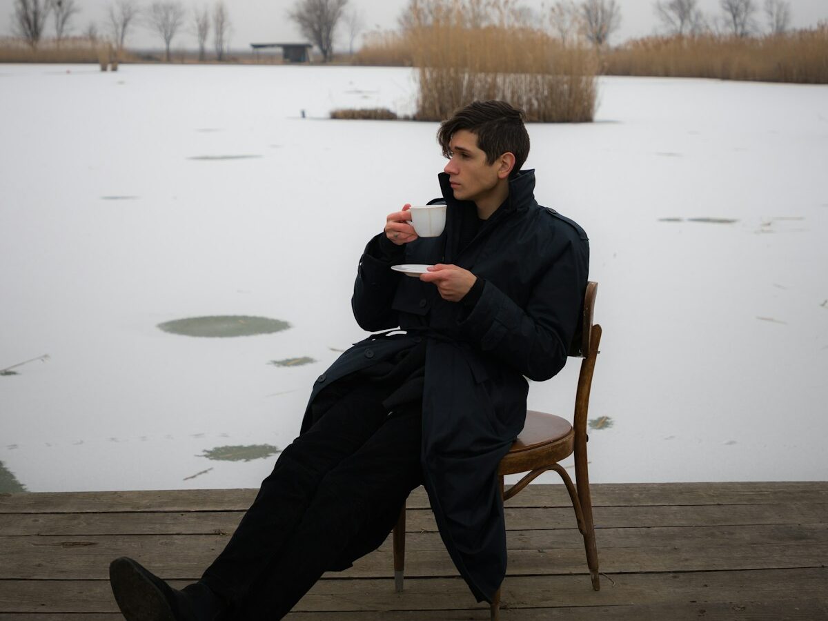 a man sitting on a wooden deck drinking a cup of coffee
