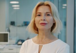 A blonde woman in a white blouse smiles