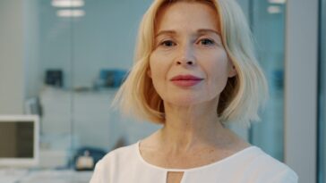 A blonde woman in a white blouse smiles