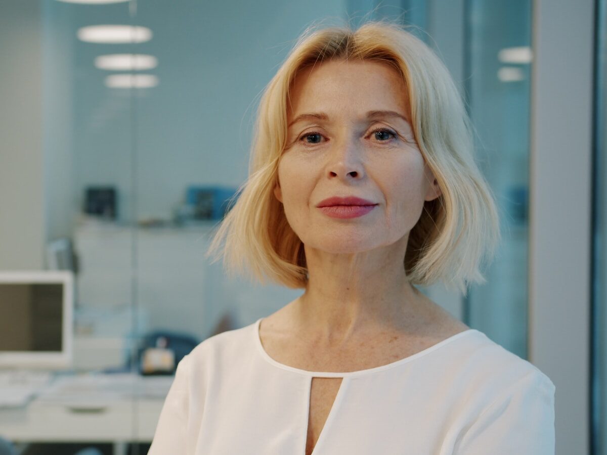 A blonde woman in a white blouse smiles
