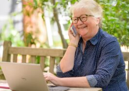 a woman on her phone while sitting at a table with a laptop