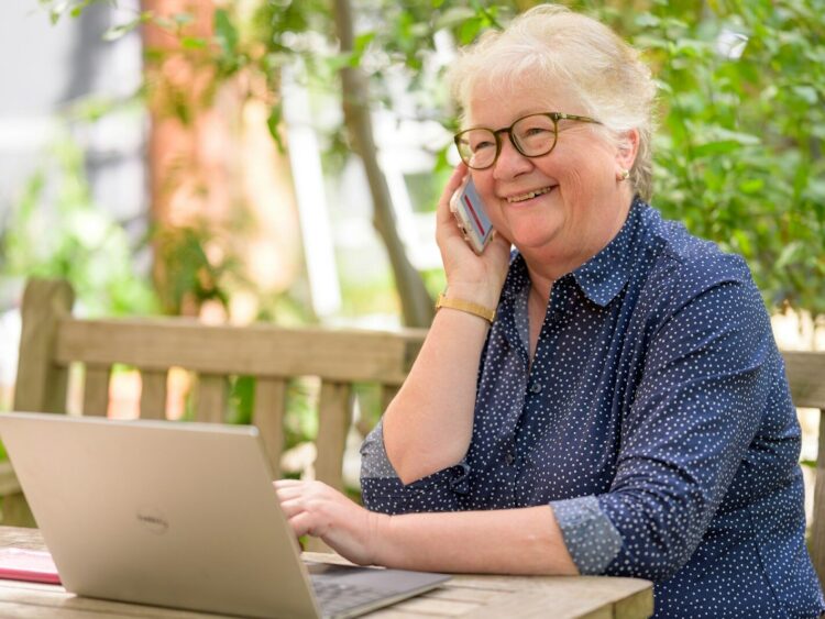 a woman on her phone while sitting at a table with a laptop