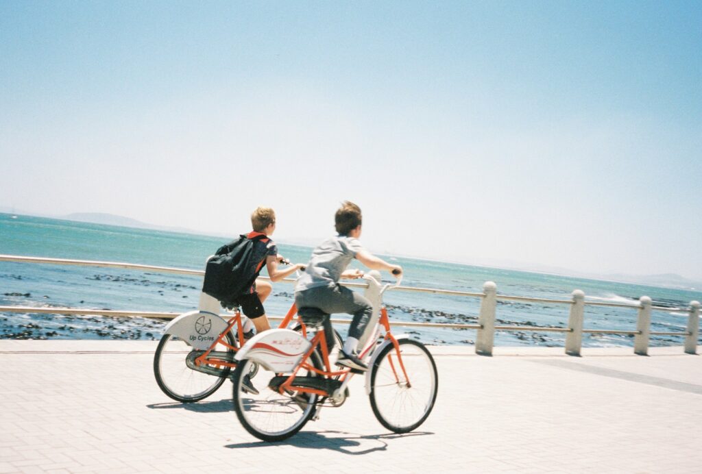 2 women riding on red bicycle on white sand beach during daytime