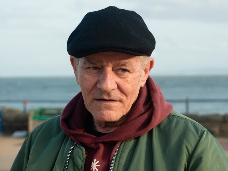 an old man wearing a black hat and a green jacket